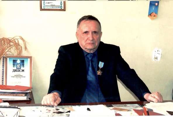 Виктор Михайлович Инюшин сидит за рабочим столом в кабинете КазГУ
